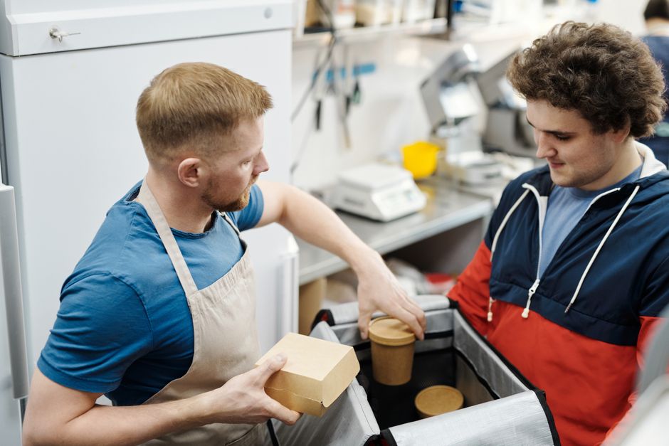 Two young men preparing food delivery orders in a small business kitchen.